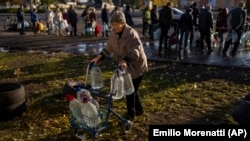 75-летняя Екатерина толкает ходунки с пластиковыми бутылками после того, как наполнила их из бака. Николаев, Украина 24 октября 2022 года