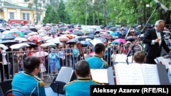 Алматыда Жеңіс күні әскери оркестрдің өнерін тамашалаған көрермен жұрт сіркіреген жаңбырдан қолшатырмен қорғанып тұр. 9 мамыр 2015 жыл.