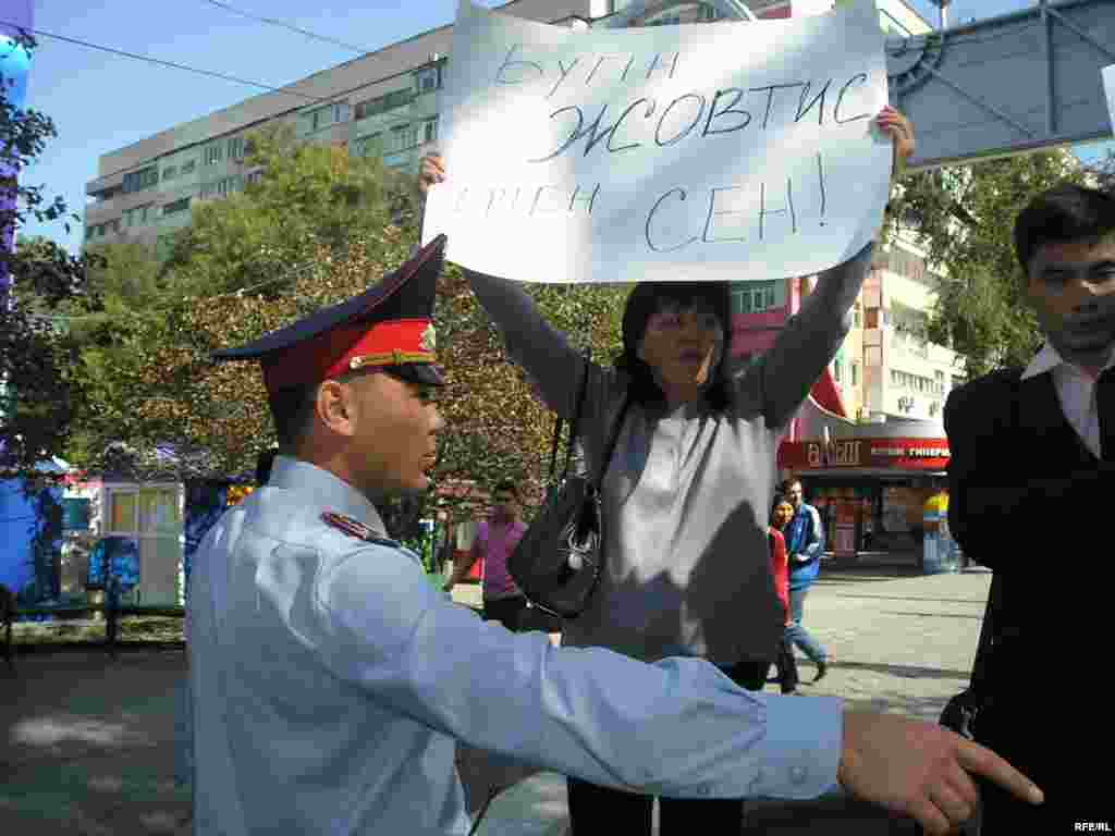 Полиция Жовтисті қолдау акциясына бөгеп жасады. - Жовтисті жақтаушы Ольга Оразбекова "Бүгін - Жовтис, ертең - Сен!" плакатын ұстап тұр, қасындағы полиция қызметкері одан акцияны тоқтатуын талап етті. Алматының Арбаты, 30 қыркүйек 2009 жыл.